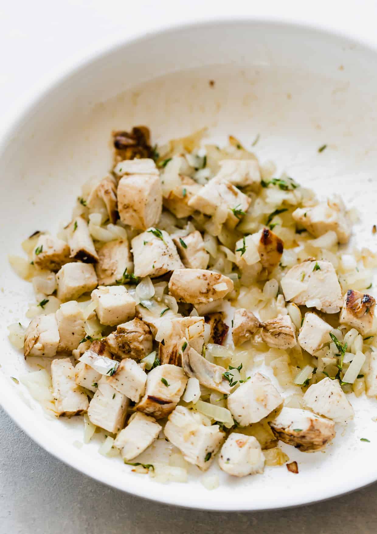 A white saute pan with diced chicken, onions, and fresh thyme. 