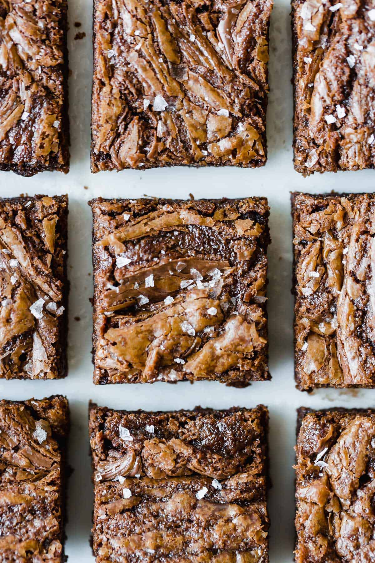 Nutella Brownies topped with flaky sea salt lined up on a white background.