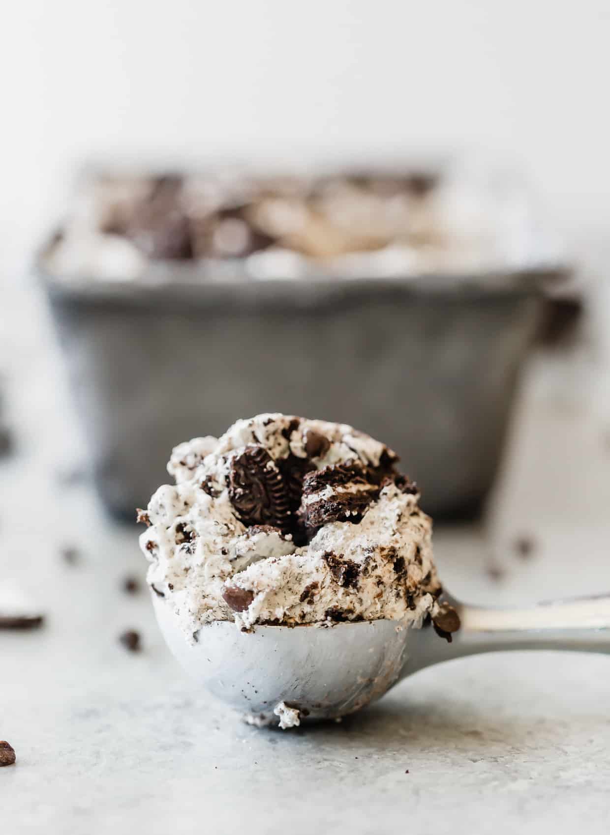 A metal ice cream scooper holding a round scoop of Oreo no churn ice cream.