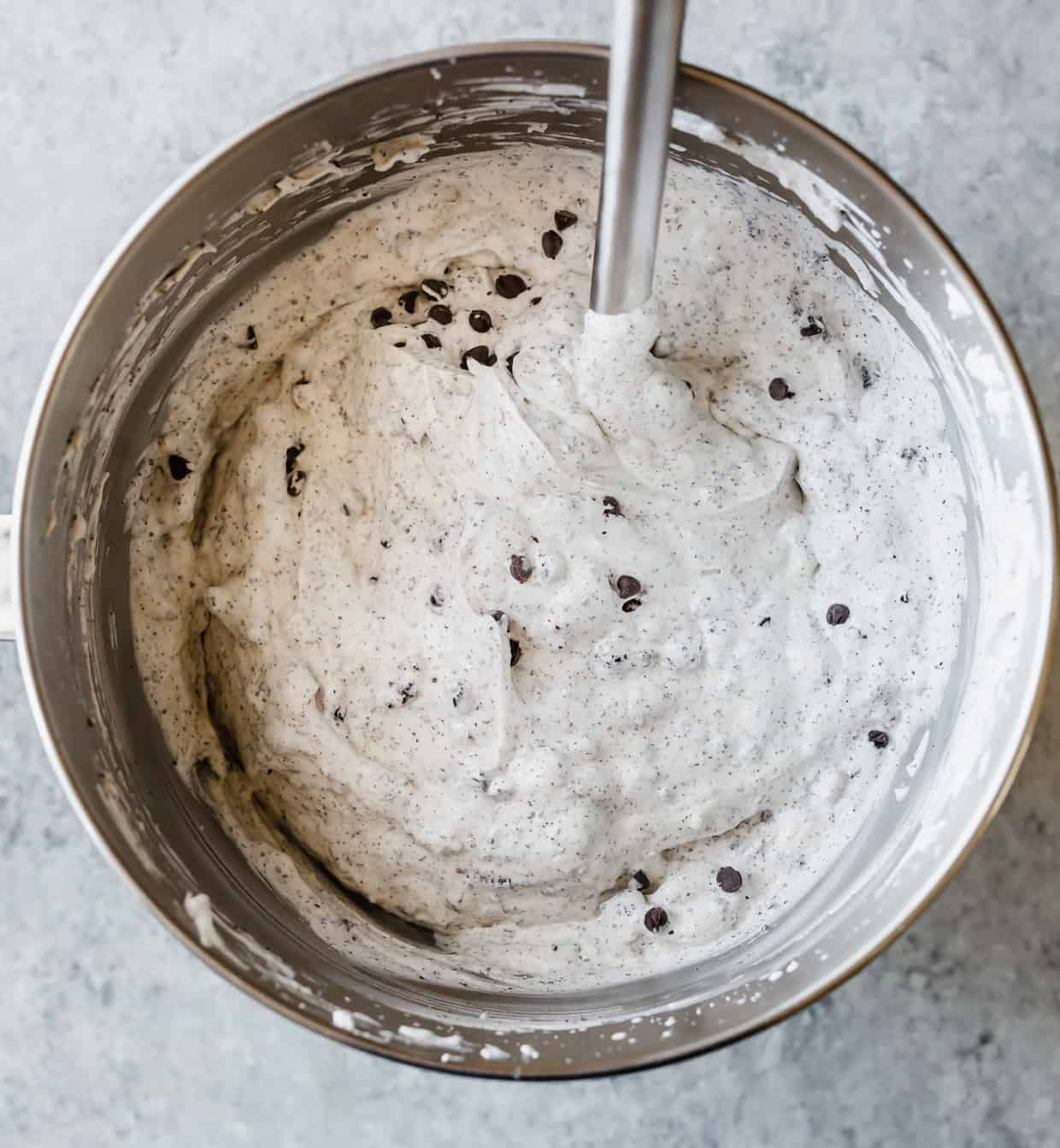 Freshly whipped cream and sweetened condensed milk in a metal bowl, with crushed Oreos and mini chocolate chips mixed into the contents.