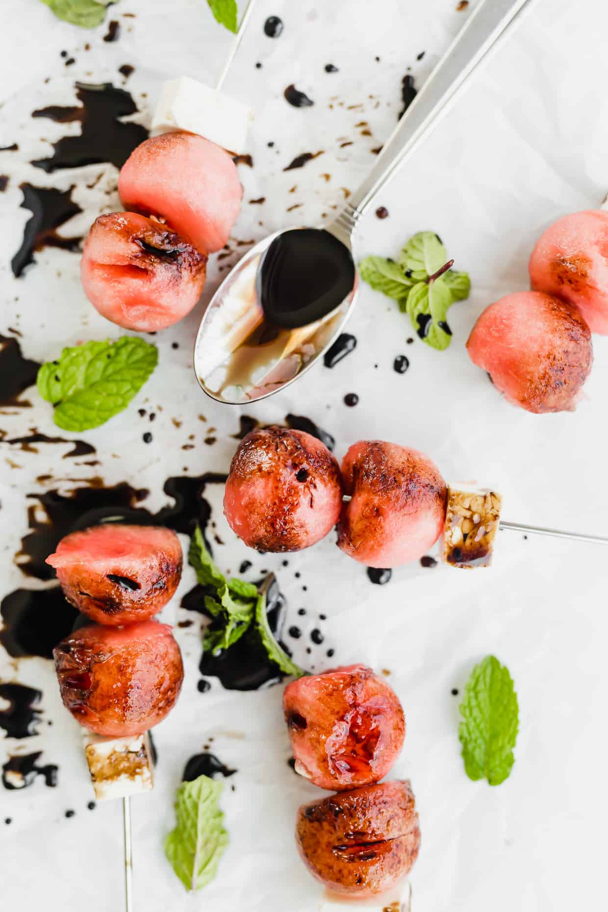 Overhead photo of 2 watermelon balls and block of feta on small skewers with balsamic reduction drizzled overtop.