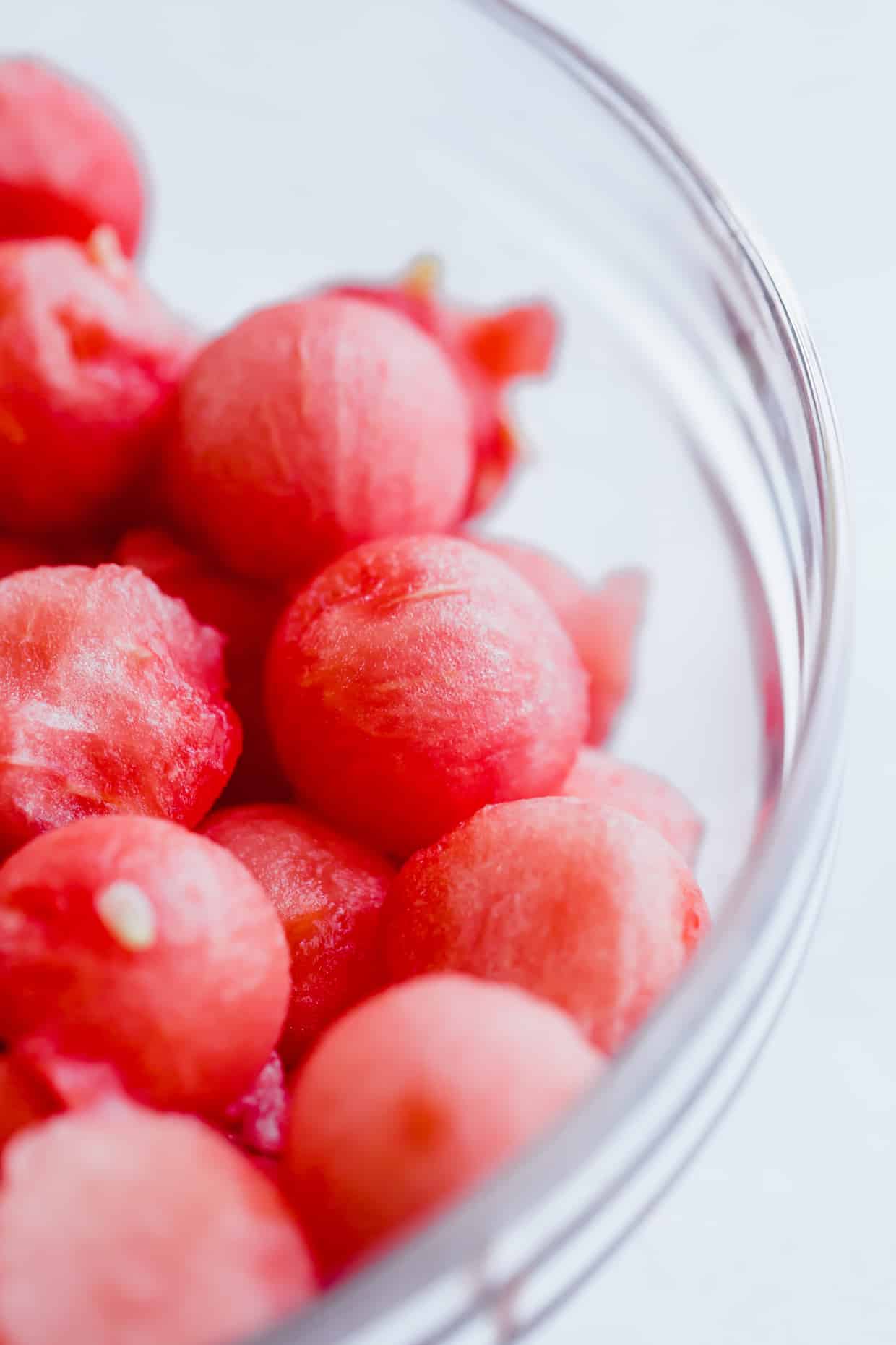 A close up photo of watermelon balls in a glass bowl.