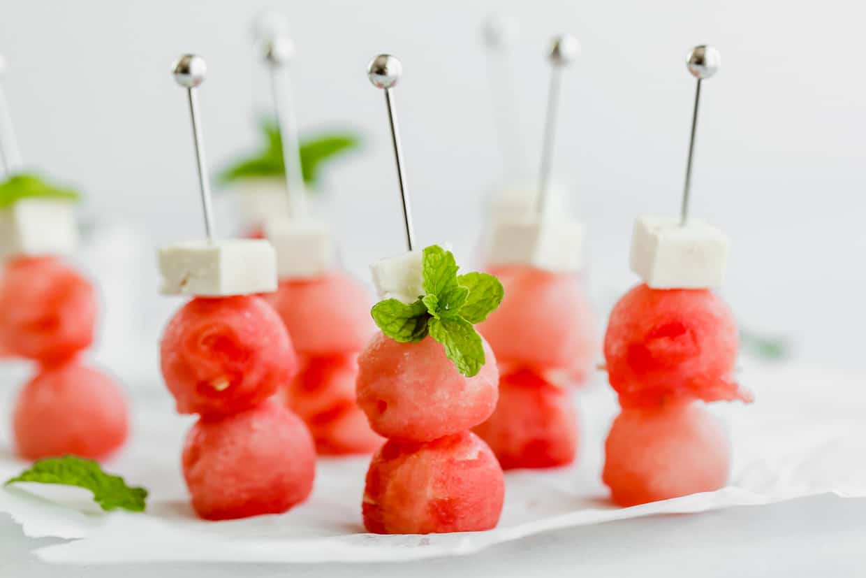 Two watermelon balls and small block of feta cheese on small metal skewers.