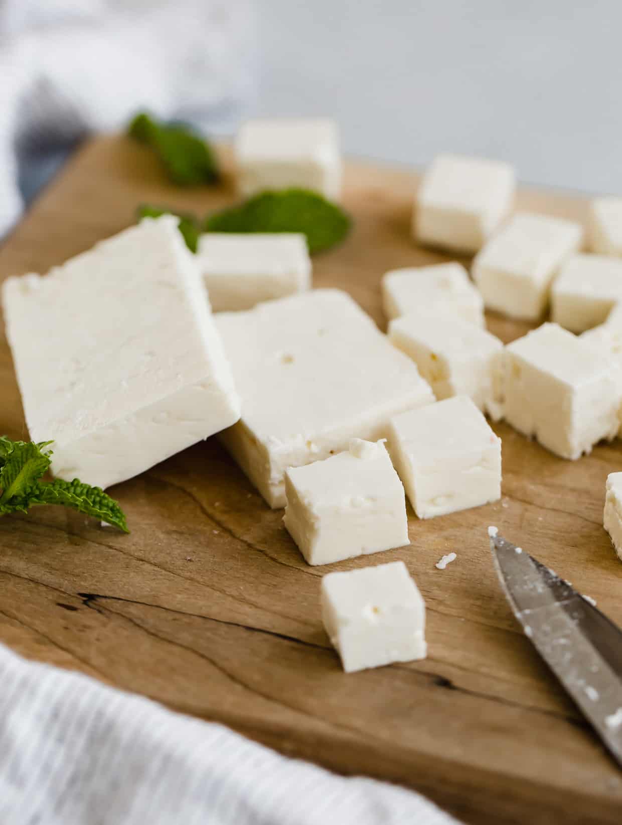 Close up photo of feta cheese on a wooden cutting board cut into small squares.