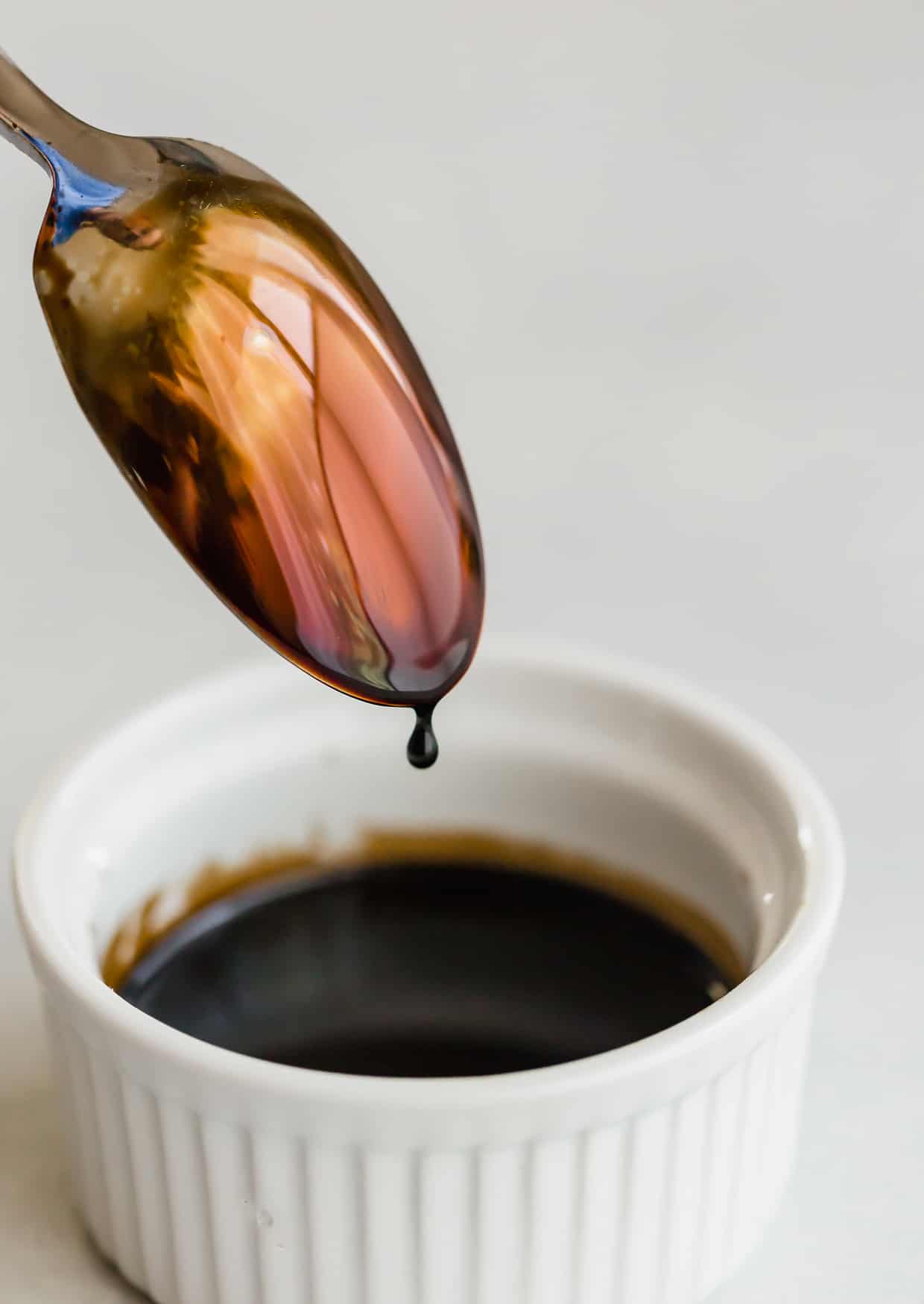 Balsamic reduction in a white bowl and a spoon just dipped into the sauce.