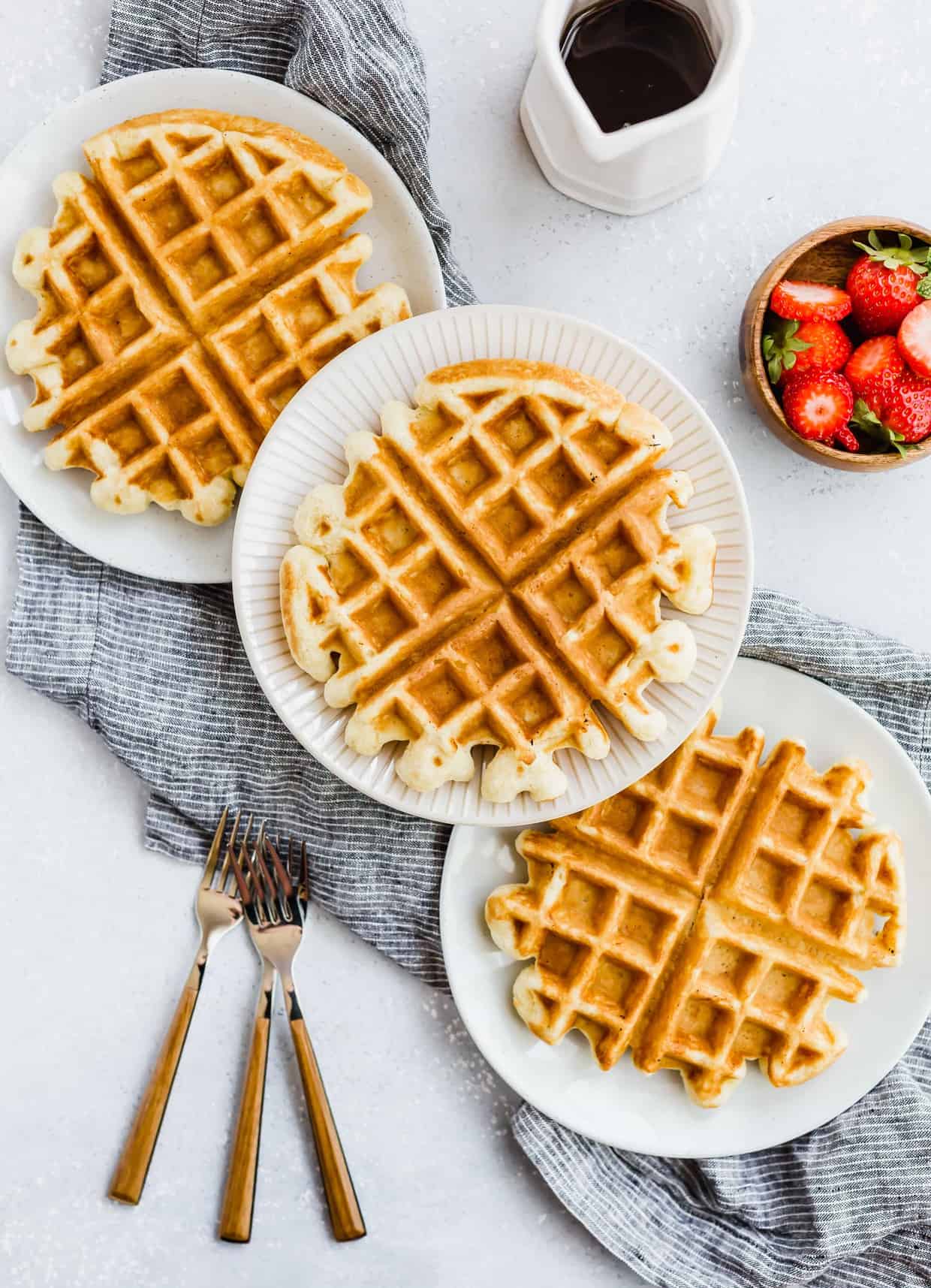 Three buttermilk waffles with three forks to the side.