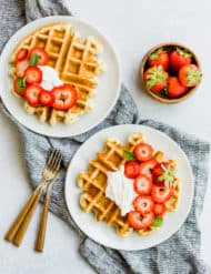 Overhead view of two buttermilk waffles topped with cream and strawberries.