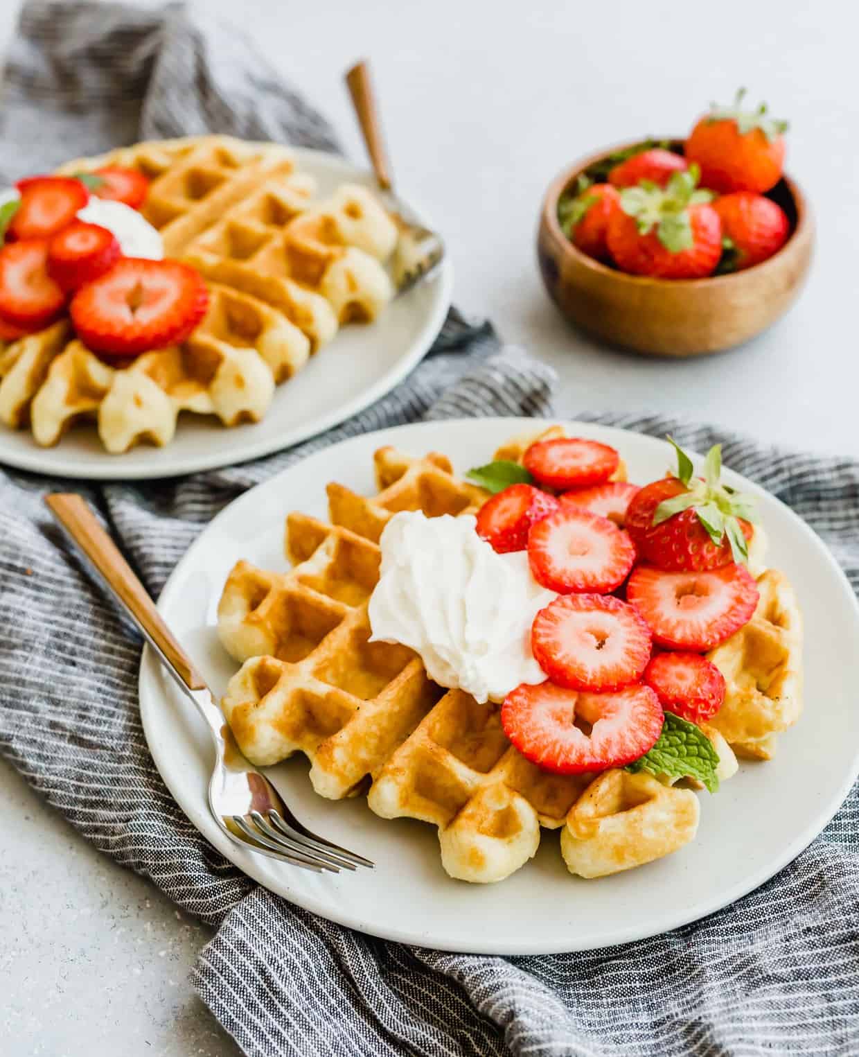 A buttermilk waffle with whipped cream and chopped strawberries on top.