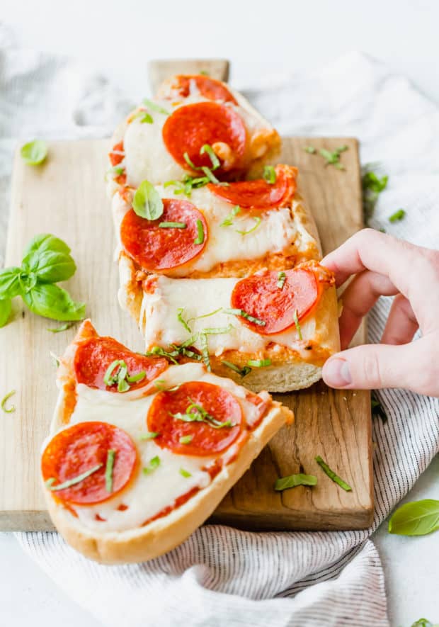 French bread pizza on a cutting board, topped with pepperoni and fresh basil.