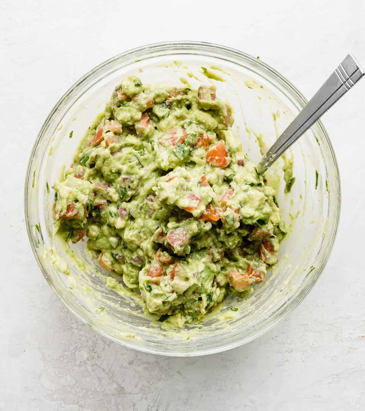 A glass bowl full of the Best Guacamole Recipe against a white background.