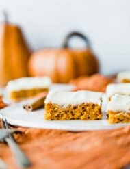 Pumpkin bars with cream cheese frosting with a pumpkin in the background.