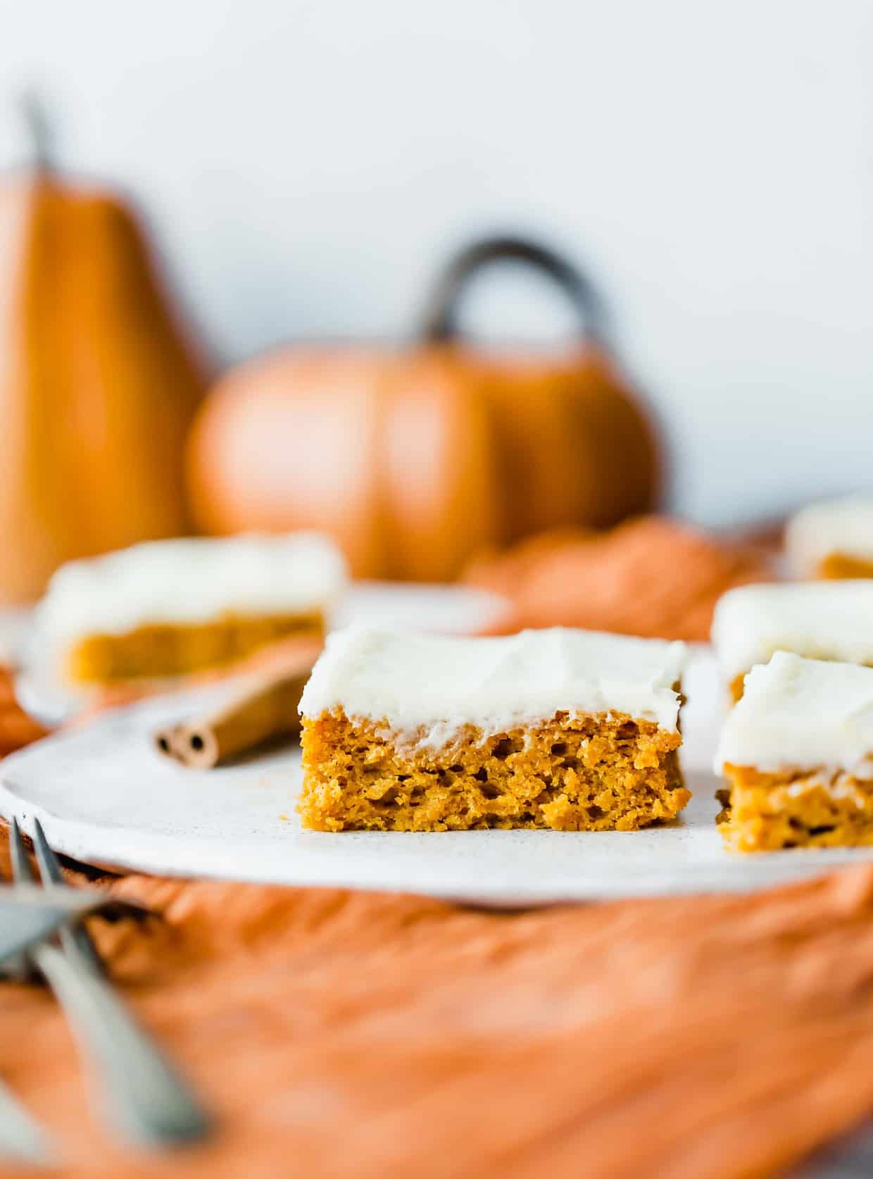 Pumpkin bars with cream cheese frosting with a pumpkin in the background.