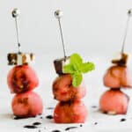 Three Watermelon Feta Skewers with balsamic reduction overtop.