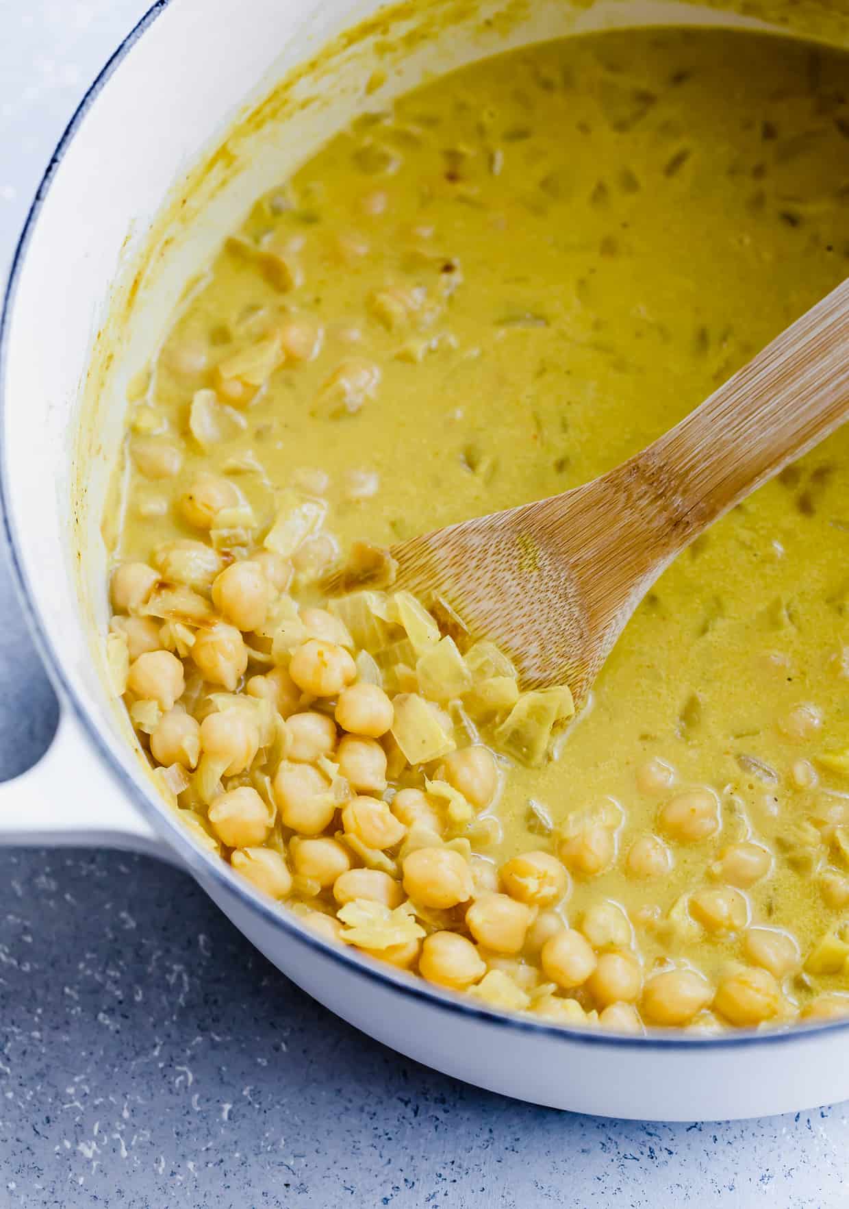Chickpea curry in a white pot, with a wooden spoon lifting out some chickpeas.
