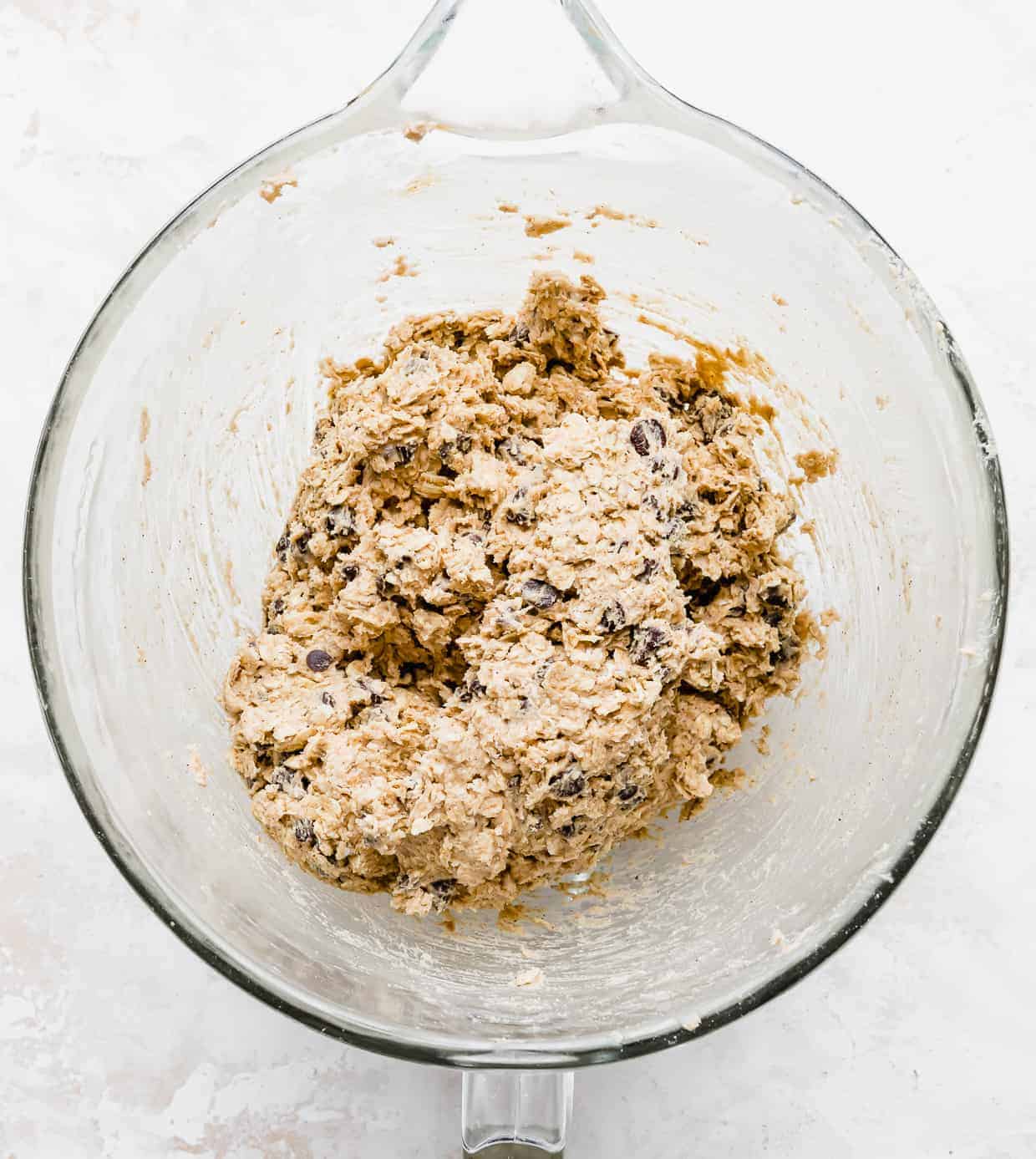 Oatmeal Chocolate Chip Cookie dough in a glass bowl against a white background.