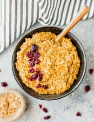 Overhead photo of pumpkin steel cut oats in a black bowl with a garnish of craisins.