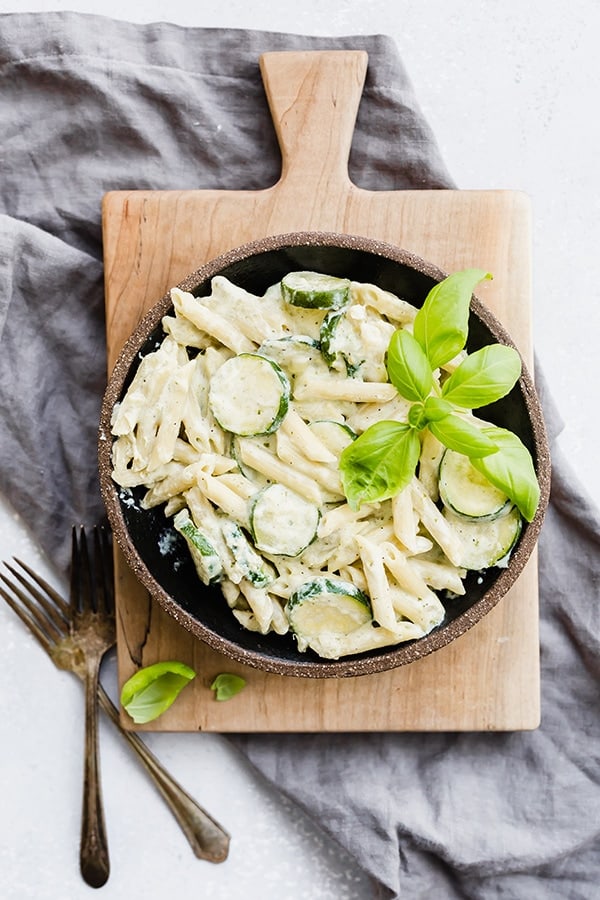 A black plate with creamy pesto pasta with zucchini and a basil garnish.