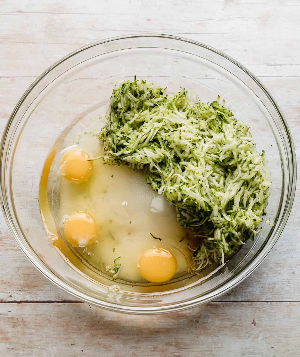 Shredded zucchini, eggs, sugar, and vanilla in a glass bowl.