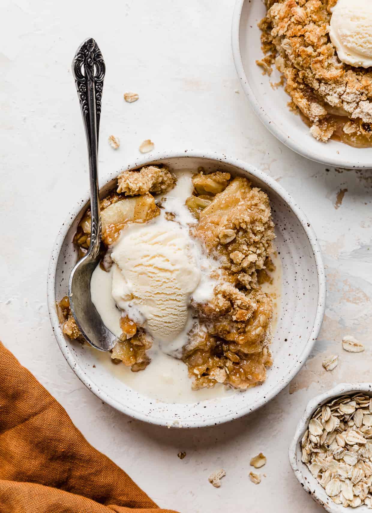 A white plate with ice cream topped apple crisp on it. 