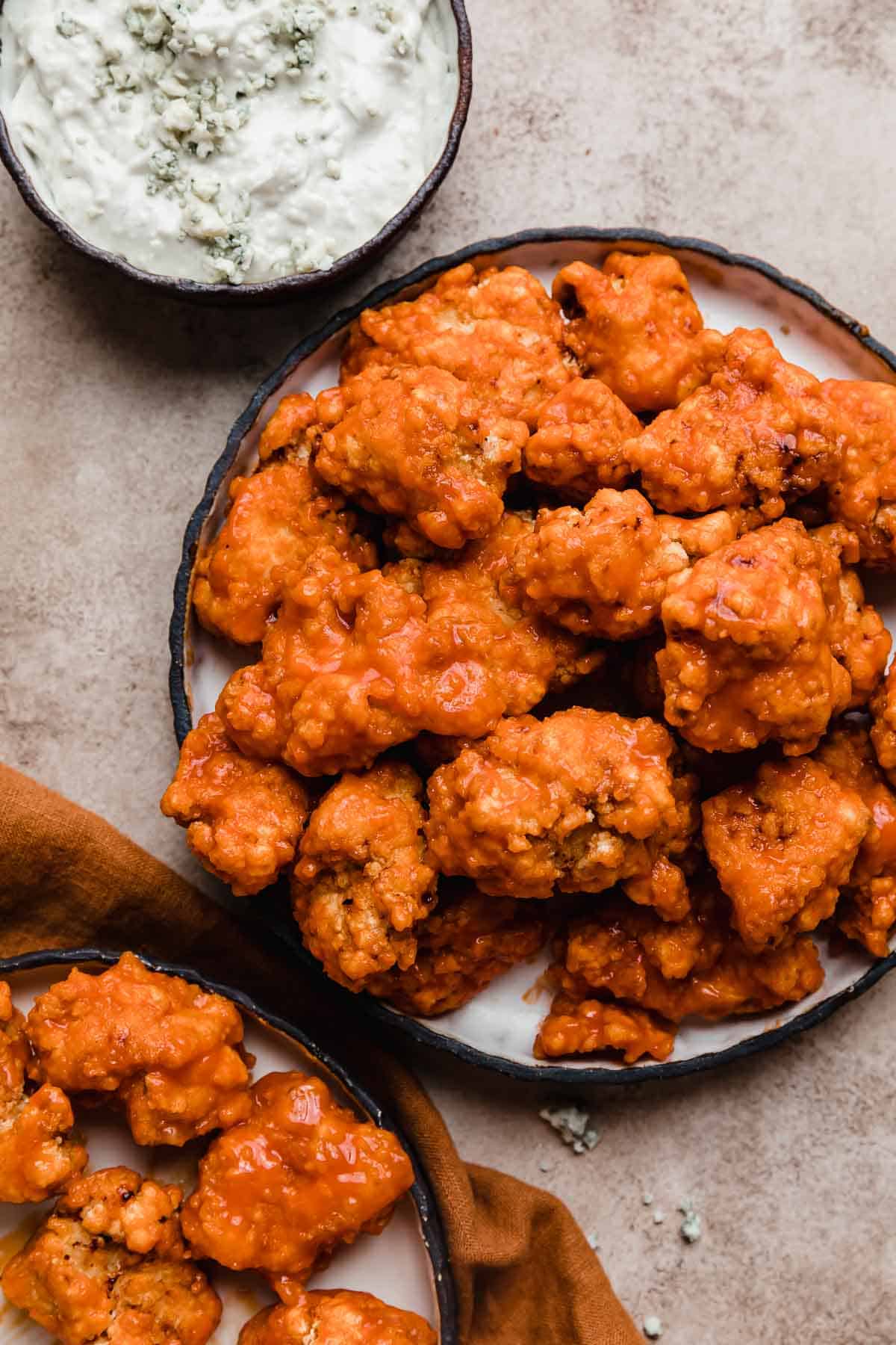 Overhead photo of Buffalo Chicken Bites on a black lined plate on a beige background.