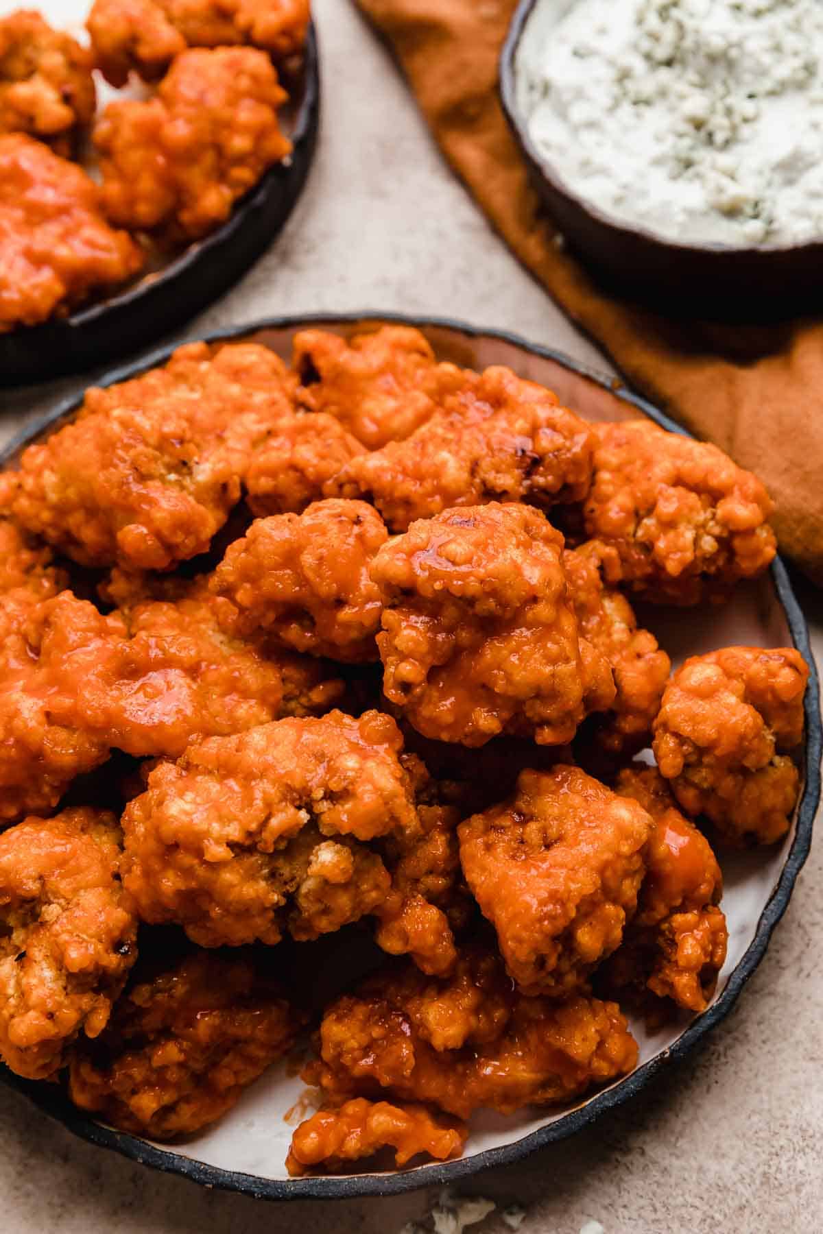 Buffalo Chicken Bites on a black rimmed plate with a blue cheese sauce in a bowl in the background.