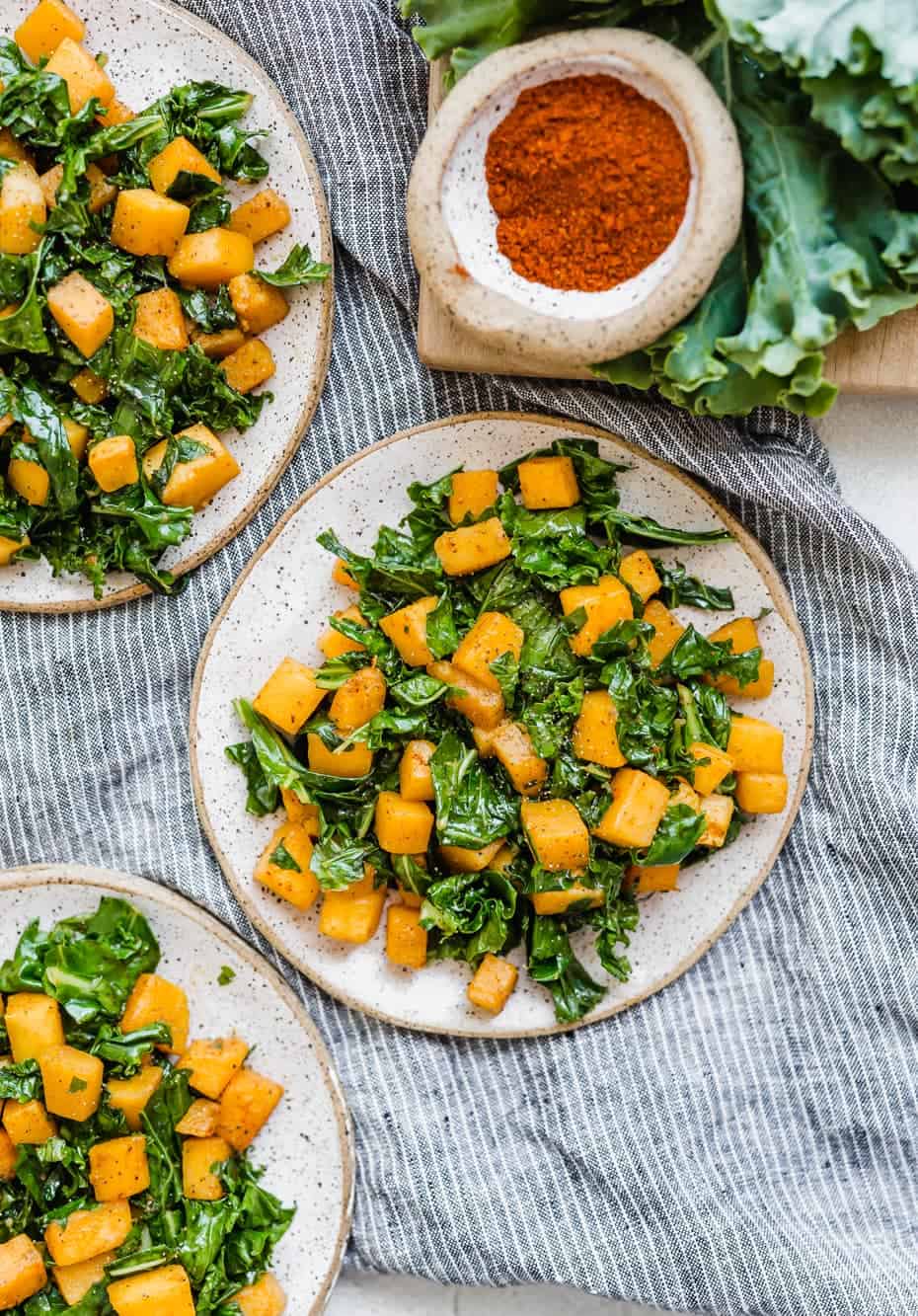 Three small plates with diced butternut squash and kale on them.