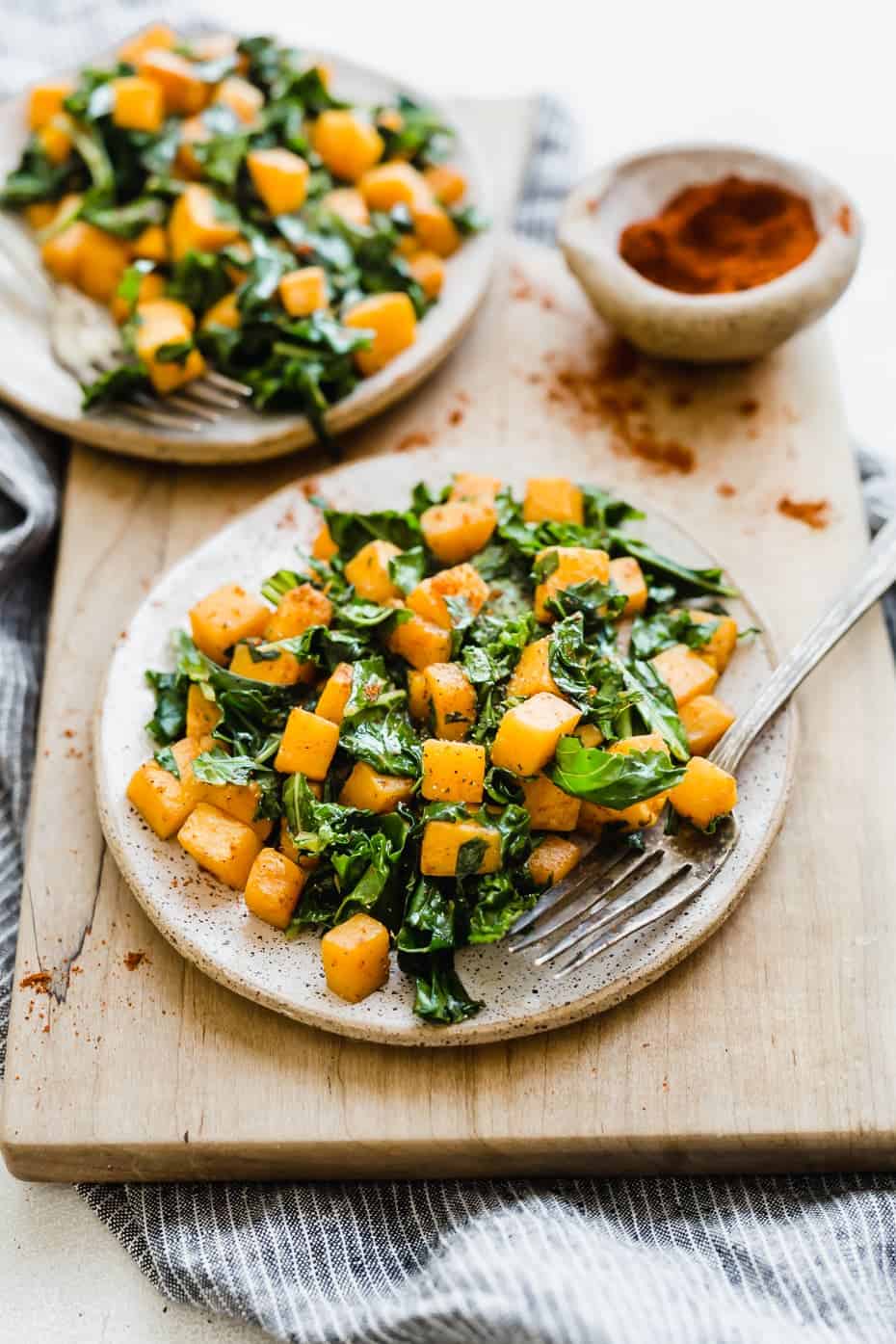 Butternut squash and kale on a plate that's sitting on a wooden cutting board.