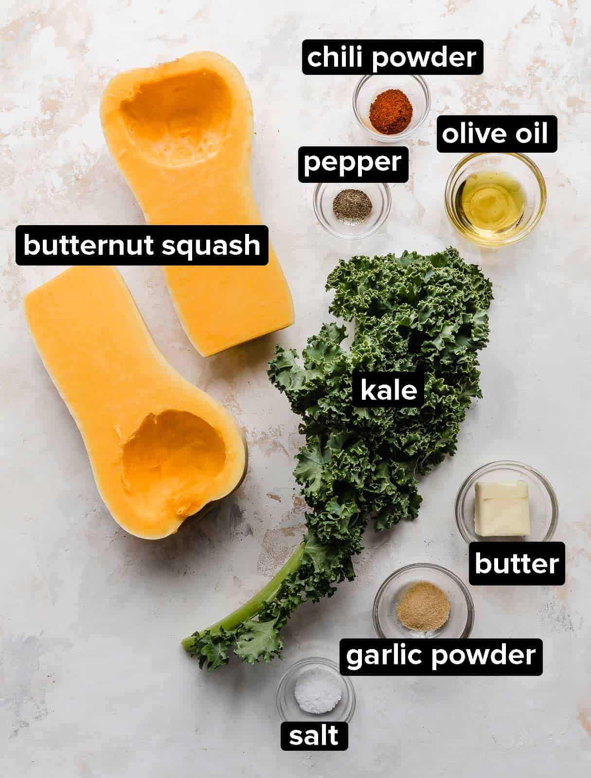 Ingredients used to make a butternut squash and kale dish, on a white textured background.