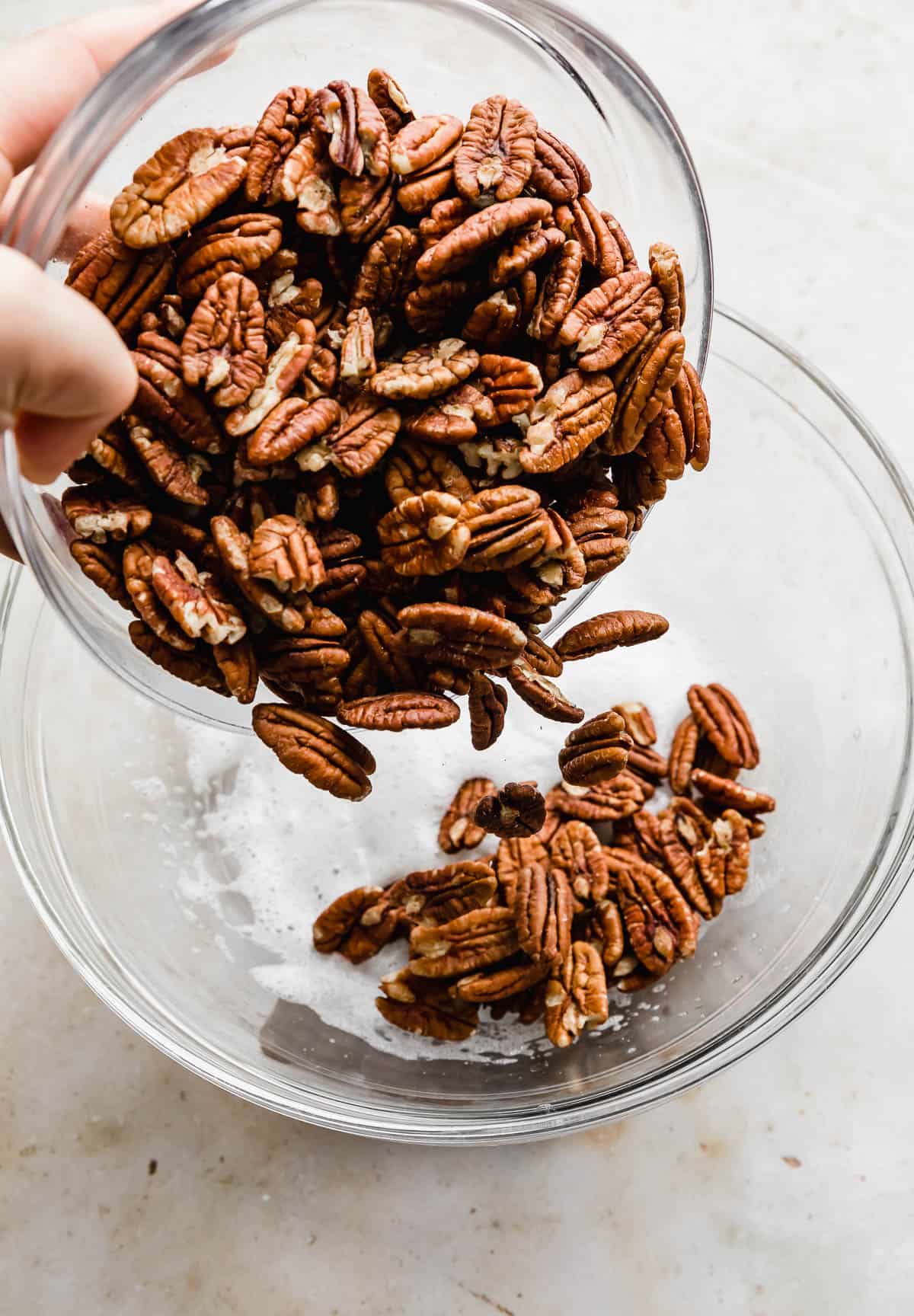 Raw pecans being poured into a glass bowl.