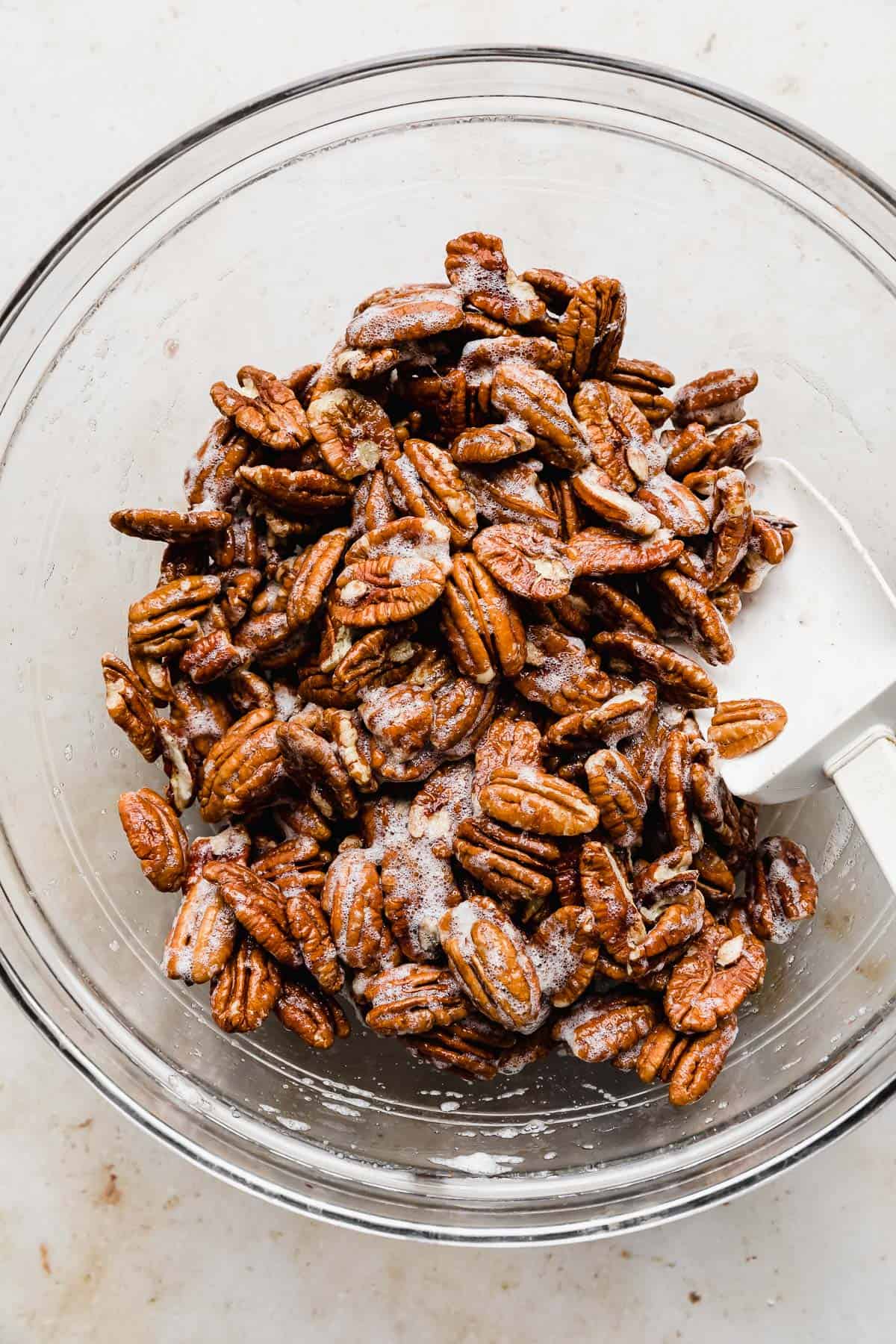 Raw pecans being mixed in frothy egg whites.