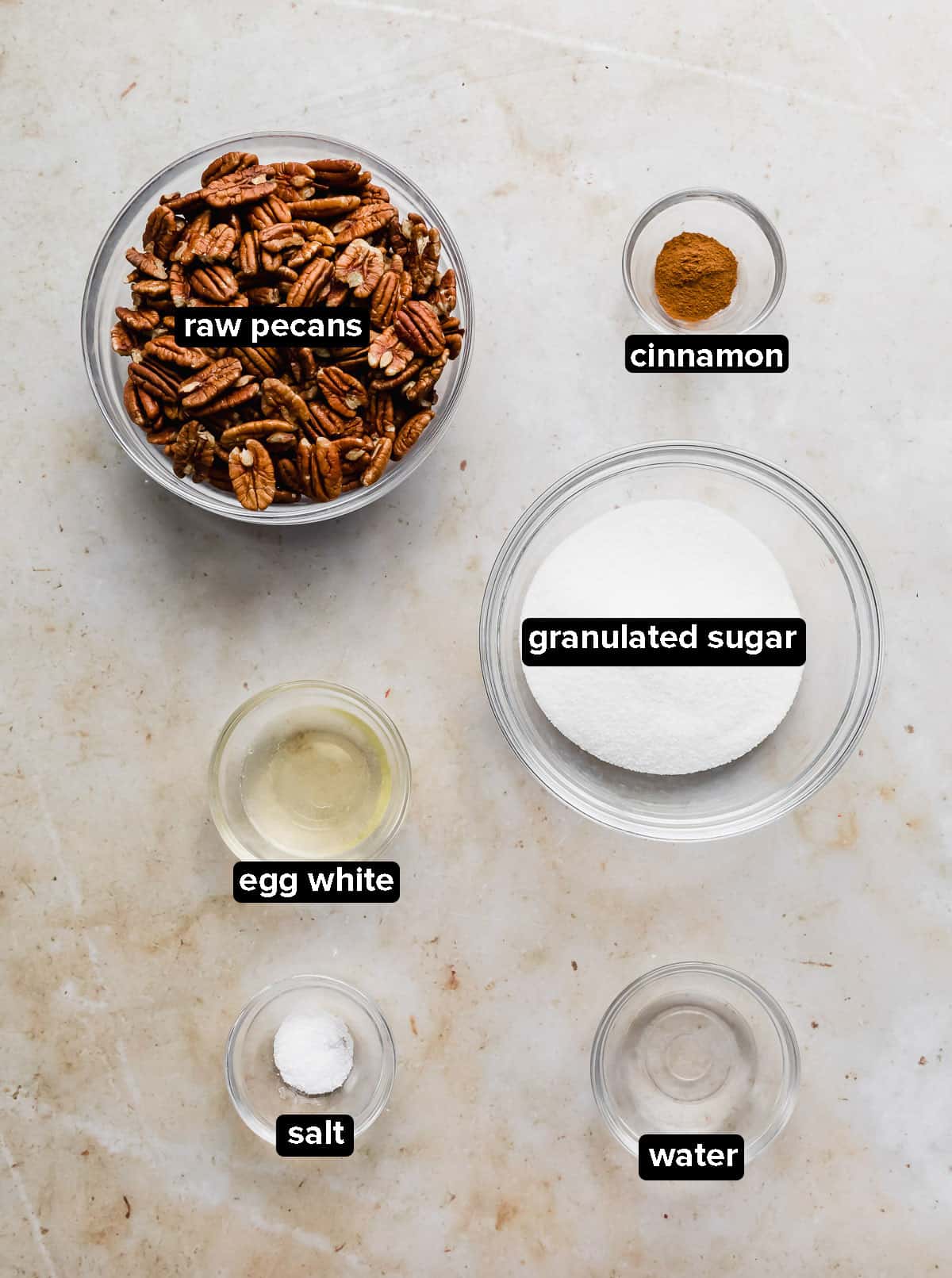 Candied Pecans recipe ingredients in glass bowls on a marble background.