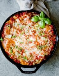 Overhead photo of lasagna baked in a large black skillet, topped with fresh basil.