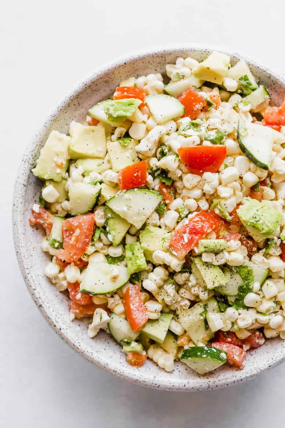 Close up image of a feta corn salad with chopped tomatoes, cucumber, corn, mint, and avocado.