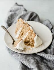 A three layered spice cake with cream cheese frosting. Small slice on a white plate.