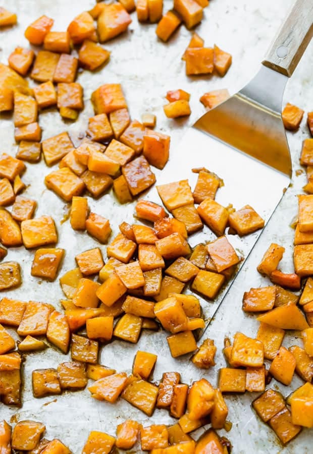 Cinnamon roasted butternut squash on a baking sheet with a metal spatula scooping some squash.