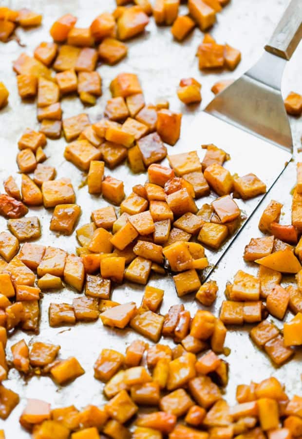 This Cinnamon Roasted Butternut Squash will be your new favorite fall side dish. The butternut squash melts in your mouth! Cinnamon roasted butternut squash on a baking sheet with a metal spatula scooping some squash.