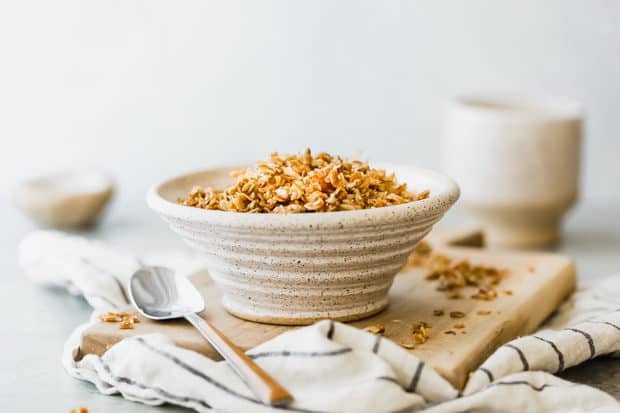 Homemade granola in a ceramic cereal bowl on a wooden cutting board.