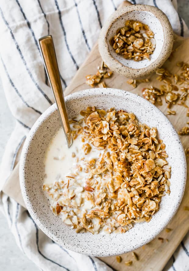 A cereal bowl full of homemade granola with milk sitting a top a white linen napkin.