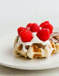 A Belgian liege waffle topped with Nutella, whipped cream, and raspberries.