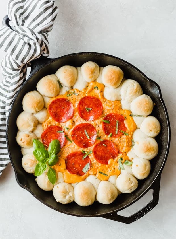 A cast iron skillet with baked pizza dough balls along the perimeter and pizza dip in the center.