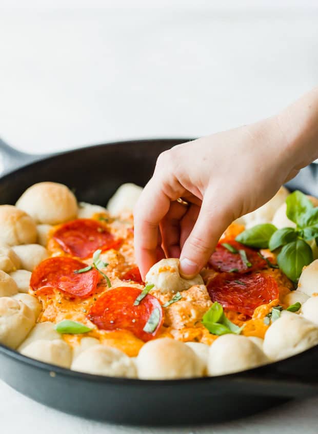 A hand dipping a pizza dough ball into the pepperoni pizza dip.