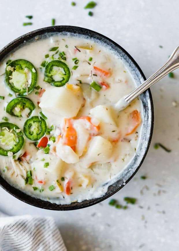 Potato pepper jack soup with a spoon in the bowl and sliced jalapeños for garnish.