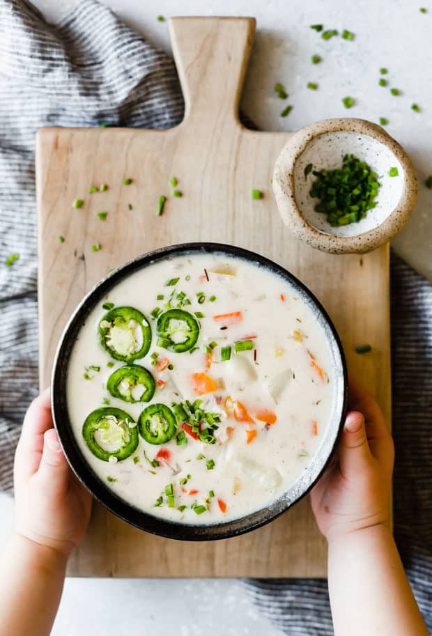 Potato pepper jack soup in a black bowl on a wooden cutting board with a young boys hands cradling the bowl.