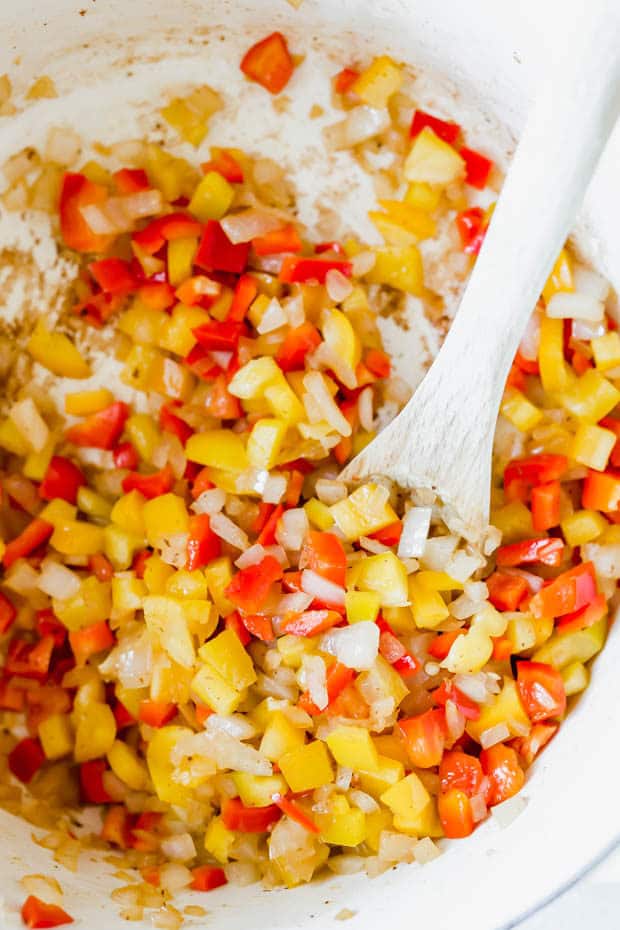 Diced onion, red pepper, and yellow pepper in a white dutch oven.