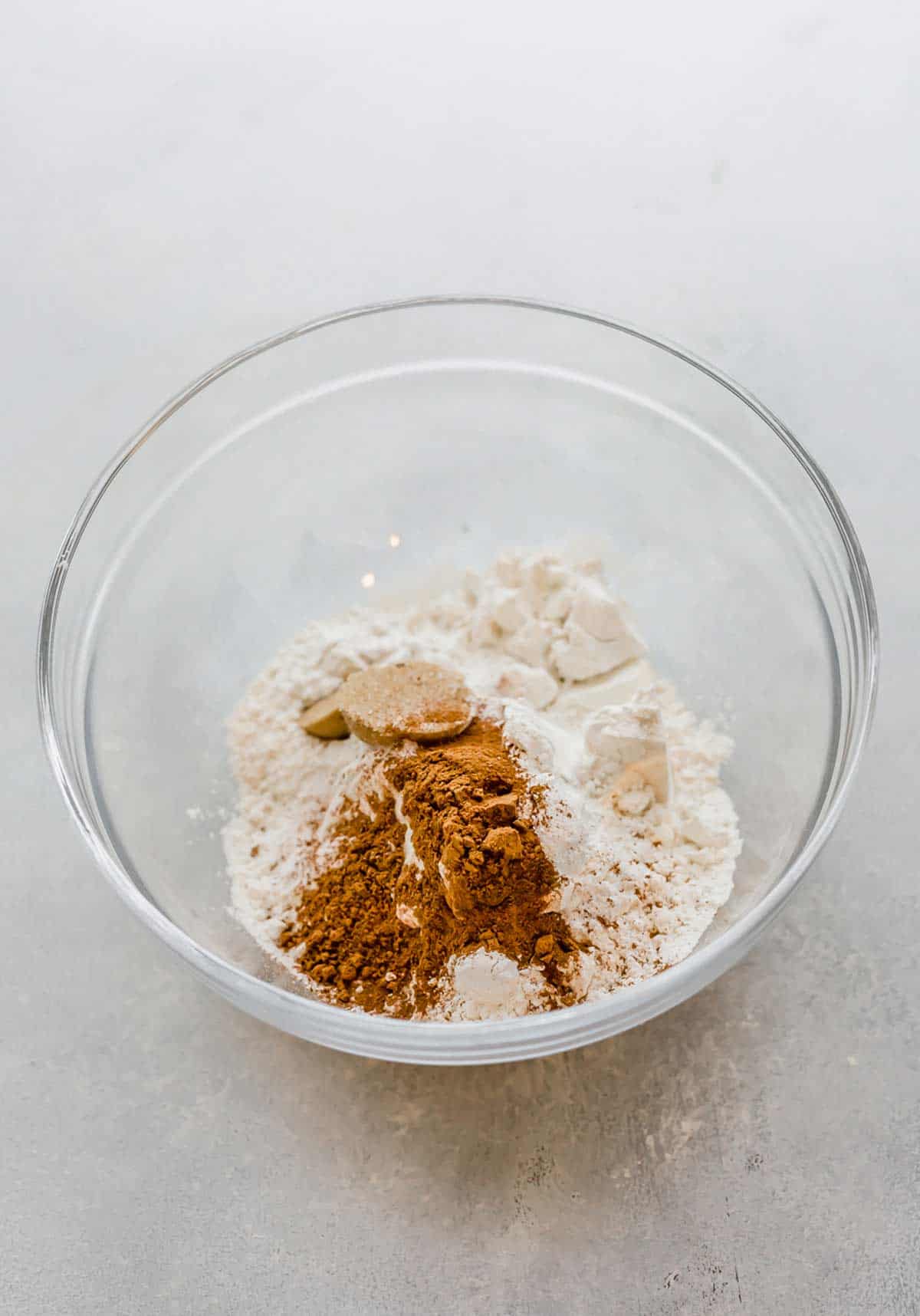 Dry ingredients used to make pumpkin pancakes, in a glass bowl on a light gray background.
