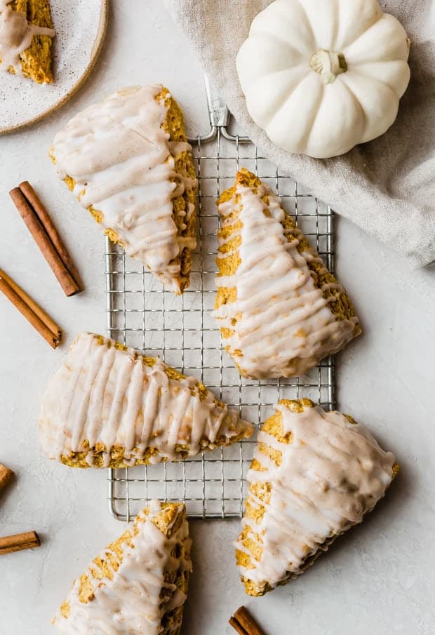 Overhead photo of pumpkin scones with a spiced glaze on a wire rack with cinnamon sticks.