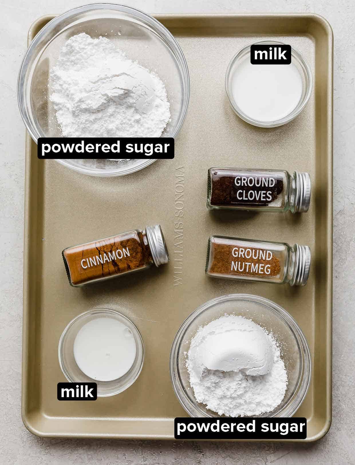 Pumpkin scone spiced glaze ingredients on a baking sheet: powdered sugar, milk, cinnamon, cloves, and nutmeg. 