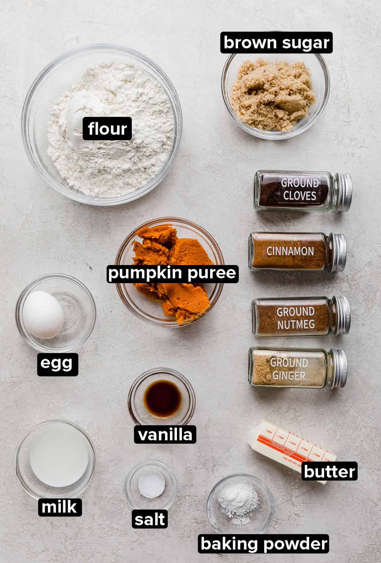 Pumpkin scones ingredients portioned into glass bowls on a light gray background.