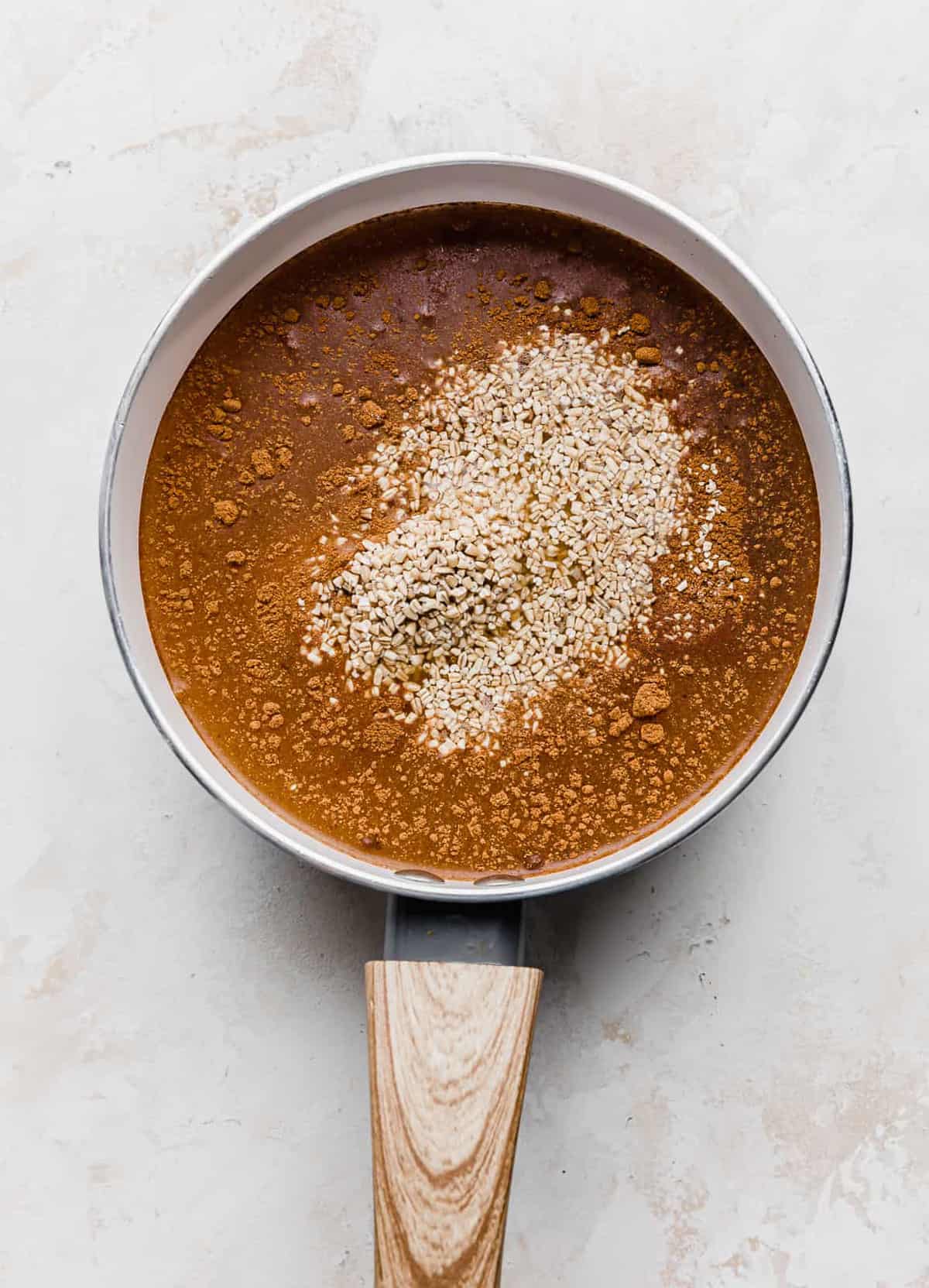 Raw steel cut oats in a white saucepan amongst a amber colored liquid.
