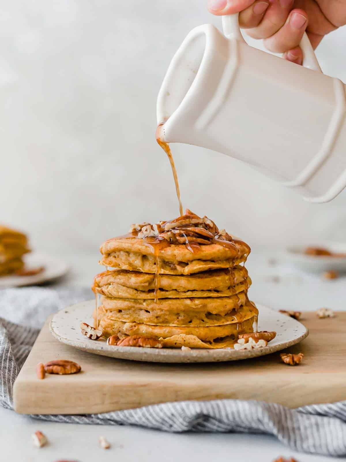 Homemade pecan pancakes syrup being poured over a stack of fluffy pumpkin pancakes.